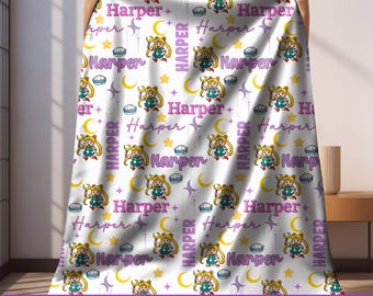 May include: White blanket with a repeating pattern of a cartoon character, moons, stars, and the name "Harper" in purple. The blanket has a purple border with the text "CUSTOM NAME & COLOR".