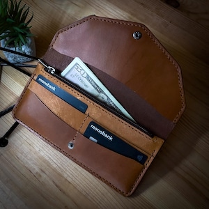 May include: A brown leather wallet with a zippered closure. The wallet is open and contains a $50 bill and two black cards with the text "monobank" printed on them.