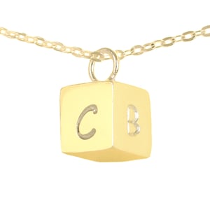 May include: Gold necklace with a cube pendant featuring the letters "C" and "B" engraved on the sides.