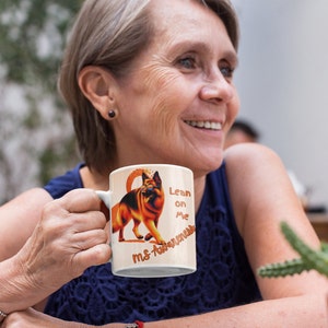 May include: A white ceramic mug featuring a German Shepherd dog illustration with the text "Lean on Me MS Awareness" in orange. The dog is depicted in shades of brown and black, wearing glasses. The mug is held by a person.