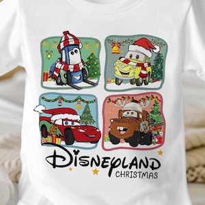 May include: White t-shirt with a Christmas themed design featuring four characters from the Disney Pixar movie Cars. The characters are Mater, Lightning McQueen, Tow Mater, and a blue car wearing a Santa hat. The text "Disneyland Christmas" is printed below the characters.