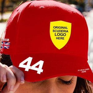 Puede incluir: Gorra de béisbol roja con un logotipo de escudo amarillo que dice "Original Scuderia Logo Here" y el número "44" en blanco en la parte delantera. La gorra también tiene una pequeña bandera de la Unión Jack en el lateral y el texto "Puma Logo Here" en la parte posterior.