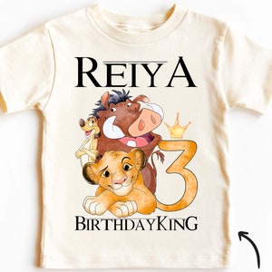 Puede incluir: Una camiseta vintage blanca con un diseño temático de El Rey León. La camiseta presenta los personajes Simba, Pumbaa y Timón. El texto "REIYA BIRTHDAY KING 3" está impreso en la camiseta.