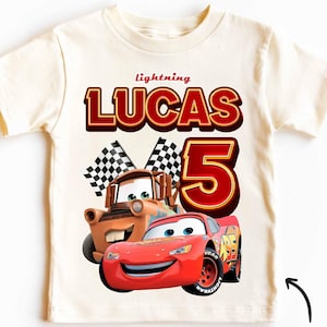 Peut inclure: Un t-shirt vintage blanc avec une image de dessin animé rouge et orange de Flash McQueen et Martin de Cars. Le t-shirt porte l'inscription "lightning LUCAS 5".