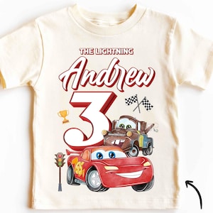 Può includere: Una maglietta vintage bianca con un design a tema Cars in rosso e nero. La maglietta presenta il testo "The Lightning Andrew 3" con un numero 3 rosso e immagini di Saetta McQueen e Cricchetto.