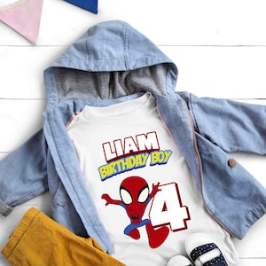 May include: White t-shirt with a red and blue Spiderman graphic, the text "Liam Birthday Boy" and the number "4". The shirt is on top of a blue denim jacket and yellow pants.