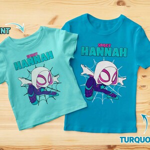May include: Two t-shirts with a graphic of a white spider-man character. The t-shirt on the left is mint green and the t-shirt on the right is turquoise. Both shirts have the text "SPIDEY HANNAH" on them.