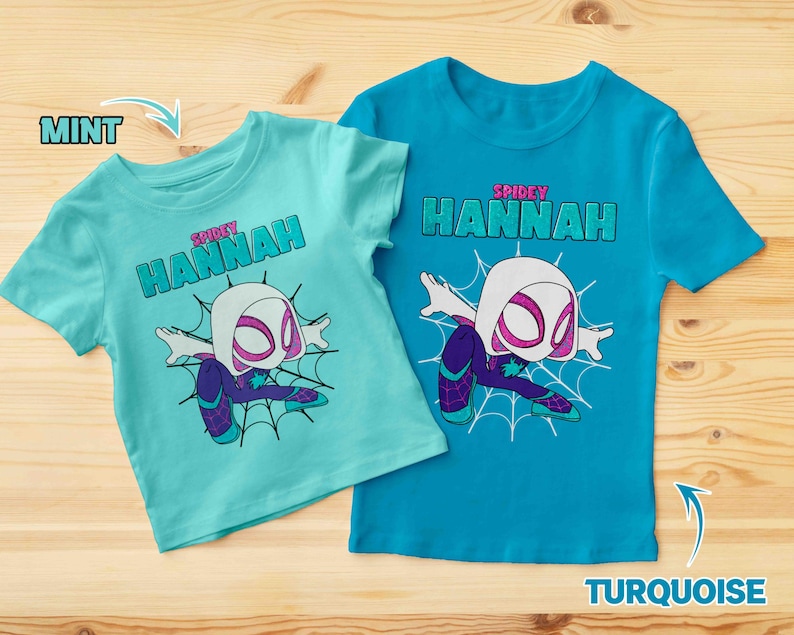 May include: Two t-shirts with a graphic of a white spider-man character. The t-shirt on the left is mint green and the t-shirt on the right is turquoise. Both shirts have the text "SPIDEY HANNAH" on them.
