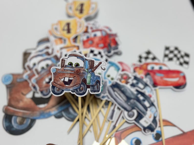 May include: A set of 12 cupcake toppers featuring characters from the Disney Pixar movie Cars. The toppers include Mater, Lightning McQueen, and other characters. The toppers are printed on cardstock and attached to wooden skewers.