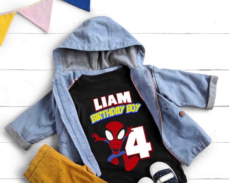 May include: Black t-shirt with a red and blue Spiderman graphic, the text "Liam Birthday Boy" in yellow and red letters, and the number "4" in white. The shirt is on top of a blue hooded jacket and yellow pants.