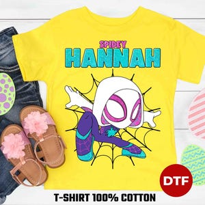 May include: Yellow t-shirt with a cartoon image of Spider-Gwen, a female superhero with white skin, a black and purple suit, and a spider web design. The text "SPIDEY HANNAH" is printed on the shirt.