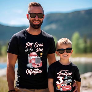 May include: Two black t-shirts with a Cars theme. The adult shirt says "Pit Crew Dad Matthew" with a red race car truck. The child's shirt says "The Lightning Andrew 3" with a red race car.