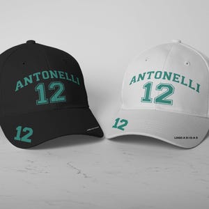 Könnte beinhalten: Zwei Baseballkappen, eine schwarze und eine weiße, mit dem Namen "ANTONELLI" und der Nummer "12" in Grün auf der Vorderseite. Die schwarze Kappe hat eine kleine italienische Flagge an der Seite und die weiße Kappe hat die Worte "LOGO SCUDERIA" an der Seite.