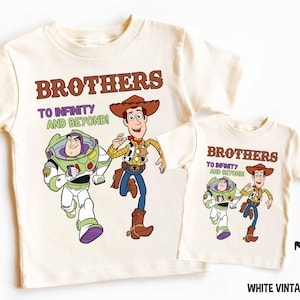 Puede incluir: Dos camisetas blancas con temática de Toy Story. La camiseta más grande presenta a Woody y Buzz Lightyear con el texto "Brothers to Infinity and Beyond!" La camiseta más pequeña presenta a Woody y Buzz Lightyear con el texto "Brothers to Infinity and Beyond!"