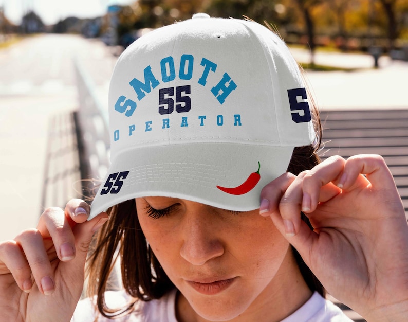 May include: White baseball cap with blue and black text that reads "SMOOTH 55 OPERATOR 5" and a red chili pepper graphic. The number 55 is also on the side of the cap.