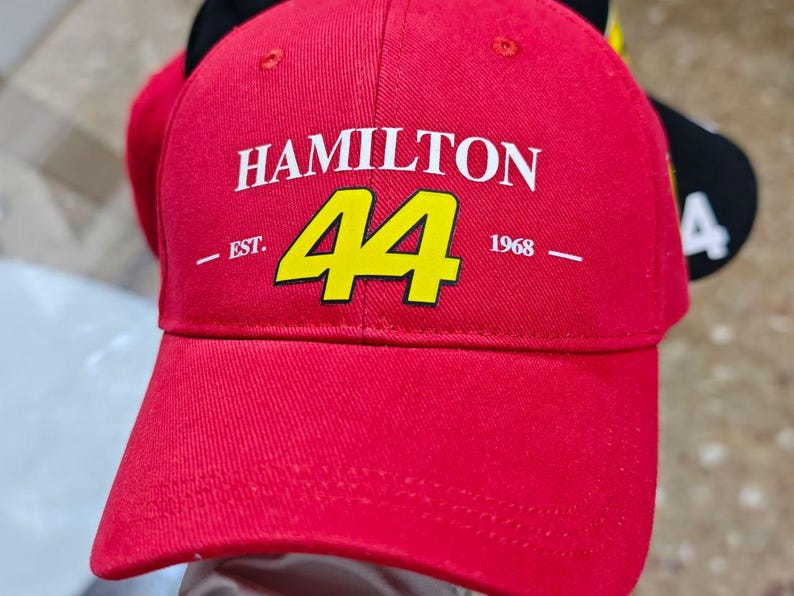 May include: Red baseball cap with a white "HAMILTON" logo and a yellow number "44" in the center. The text "EST. 1968" is printed below the number.