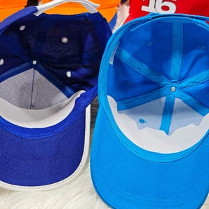 May include: Two baseball caps, one blue and one light blue, are shown from the inside. Both caps have a white brim.