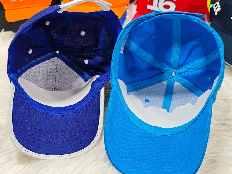 May include: Two baseball caps, one blue and one light blue, are shown from the inside. Both caps have a white brim.