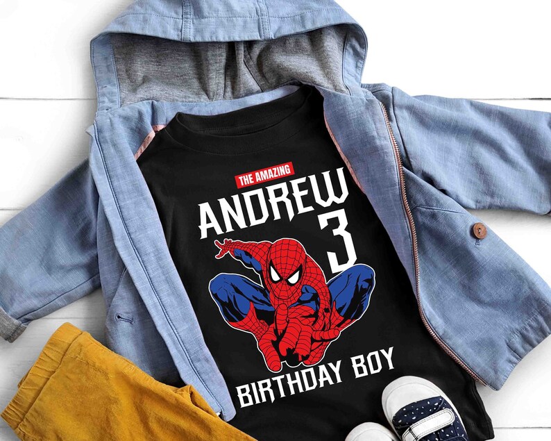 Op de afbeelding: Zwart T-shirt met een rode en blauwe Spiderman-afbeelding, de tekst "The Amazing Andrew 3 Birthday Boy" en een blauw denim jack.