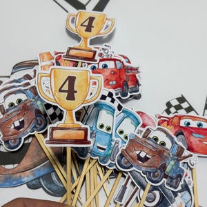May include: A set of 10 cupcake toppers featuring cartoon characters from the Cars movie franchise. The toppers include Mater, Lightning McQueen, and a trophy with the number 4 on it. The toppers are printed on cardstock and attached to wooden skewers.