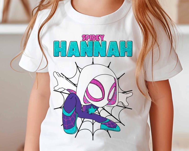May include: White t-shirt with a graphic of Spider-Gwen, a female superhero, in a white and purple suit. The text "SPIDEY HANNAH" is printed on the shirt in turquoise glitter.