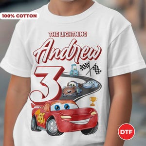 May include: White t-shirt with a red, white, and blue Cars themed design. The shirt says "The Lightning Andrew 3" and features Lightning McQueen, Mater, and other Cars characters. The shirt is 100% cotton.