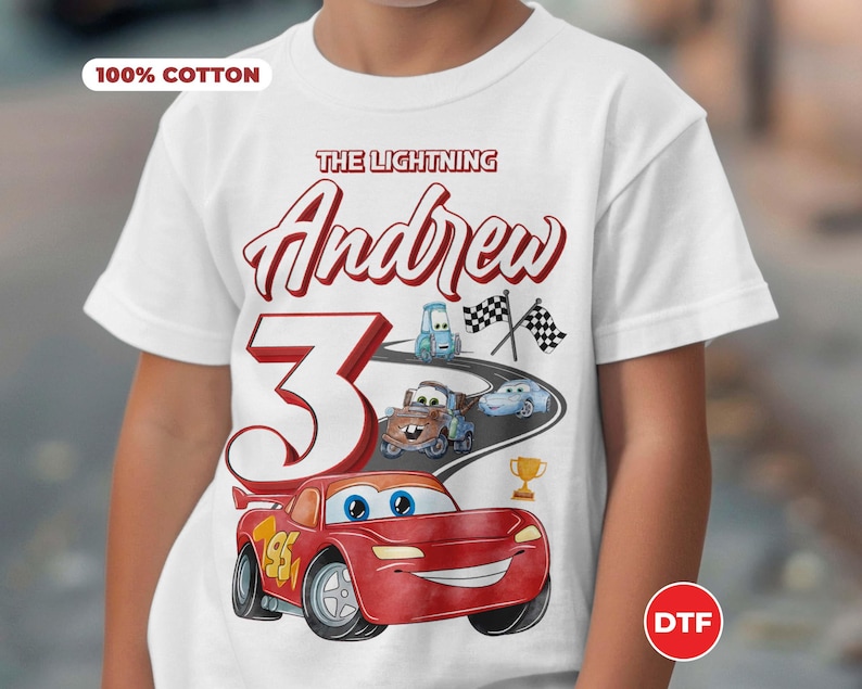 May include: White t-shirt with a red, white, and blue Cars themed design. The shirt says "The Lightning Andrew 3" and features Lightning McQueen, Mater, and other Cars characters. The shirt is 100% cotton.