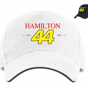 May include: White baseball cap with a black brim. The front of the cap has the text "HAMILTON" in red, "EST." and "1968" in red, and the number "44" in yellow.