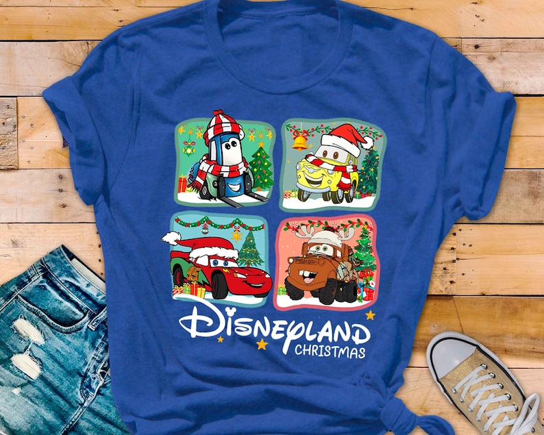 May include: Blue t-shirt with a Christmas themed design featuring characters from the Disney Pixar movie Cars. The design includes Lightning McQueen, Mater, and Tow Mater wearing Santa hats and surrounded by Christmas decorations. The text "Disneyland Christmas" is printed below the design.