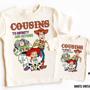Puede incluir: Dos camisetas blancas con temática de Toy Story. La camiseta más grande tiene el texto "Cousins to Infinity and Beyond!" con imágenes de Woody, Buzz Lightyear y Jessie. La camiseta más pequeña tiene el texto "Cousins to Infinity and Beyond!" con imágenes de Woody y Jessie.