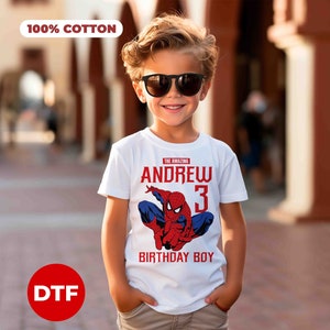 Op de afbeelding: Wit T-shirt met een rode en blauwe Spiderman-afbeelding, de tekst "The Amazing Andrew 3 Birthday Boy" en een 100% katoen label.