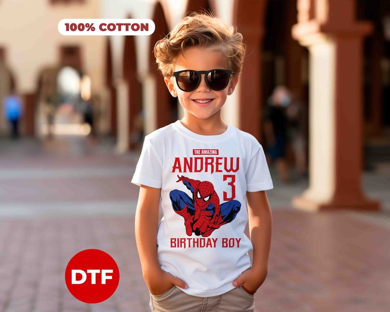 Op de afbeelding: Wit T-shirt met een rode en blauwe Spiderman-afbeelding, de tekst "The Amazing Andrew 3 Birthday Boy" en een 100% katoen label.