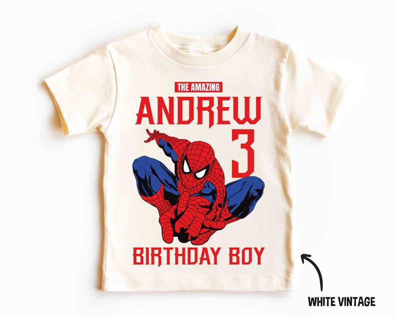 Op de afbeelding: Een wit vintage T-shirt met een rode en blauwe Spiderman-afbeelding, de tekst "The Amazing Andrew 3 Birthday Boy" in rood en blauw, en een witte pijl die wijst naar de tekst "White Vintage".