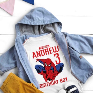 Op de afbeelding: Wit T-shirt met een rode en blauwe Spiderman-afbeelding, de tekst "The Amazing Andrew 3 Birthday Boy" en een blauw denim jack.