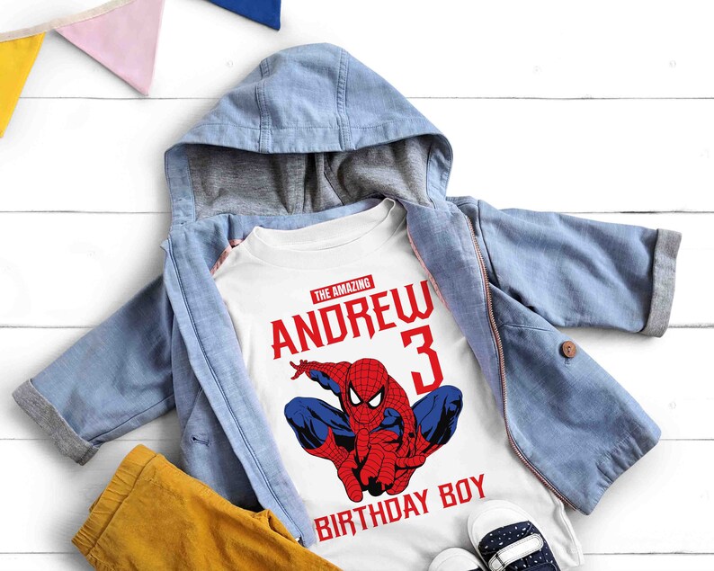 Op de afbeelding: Wit T-shirt met een rode en blauwe Spiderman-afbeelding, de tekst "The Amazing Andrew 3 Birthday Boy" en een blauw denim jack.