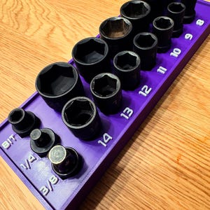 May include: A purple socket organizer with black sockets of various sizes. The organizer has white numbers indicating socket sizes, ranging from 6 to 14. Additional sockets are labeled 1/4 and 3/8. The sockets are arranged on a wooden surface.