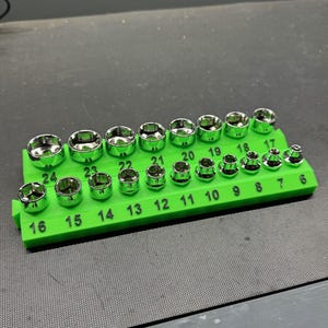 Può includere: Un set di bussole cromate disposte su un supporto verde brillante. Le bussole sono numerate da 6 a 24, con misure chiaramente indicate. Strumenti per uso meccanico o automobilistico.