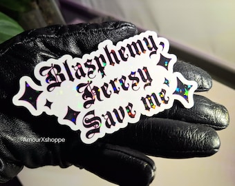 May include: A white sticker with the words "Blasphemy, Heresy, Save me" in a gothic font. The sticker has a holographic effect and is decorated with star shapes. The sticker is held by a black leather glove.