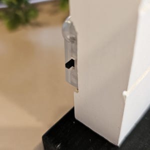 Puede incluir: Estante de madera blanca con base negra. El estante tiene un peque&ntilde;o pestillo de pl&aacute;stico transparente en el lateral.