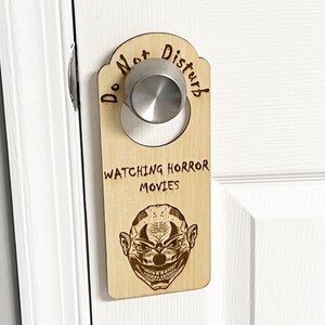 May include: Wooden door hanger with the text "Do Not Disturb" and "Watching Horror Movies". A scary clown face is featured on the hanger.