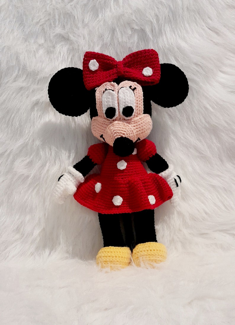 May include: A crocheted Minnie Mouse doll with a red dress with white polka dots, a black bow with white polka dots, and yellow shoes.