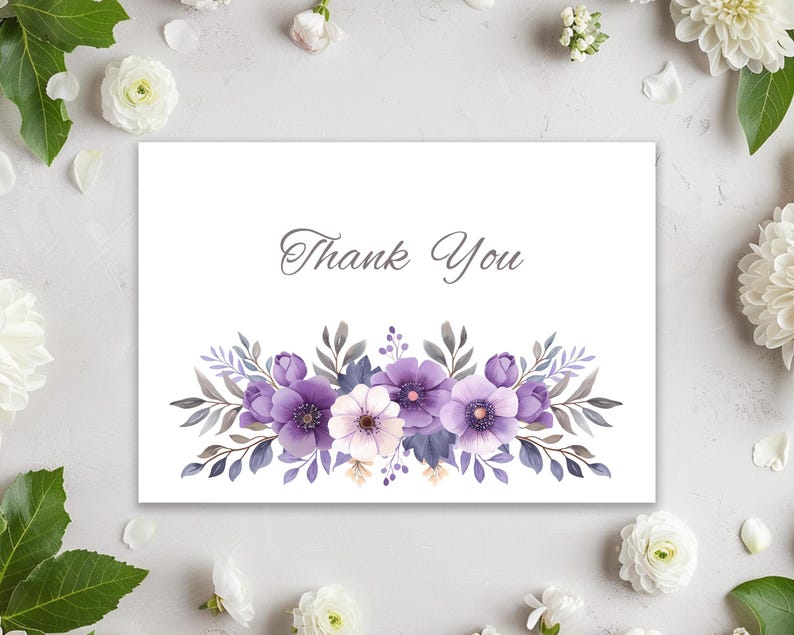 May include: A white card with the words "Thank You" in elegant script. The card features a watercolor floral design with purple, lavender, and white flowers, and gray-green leaves. The card is surrounded by white flowers and green leaves.