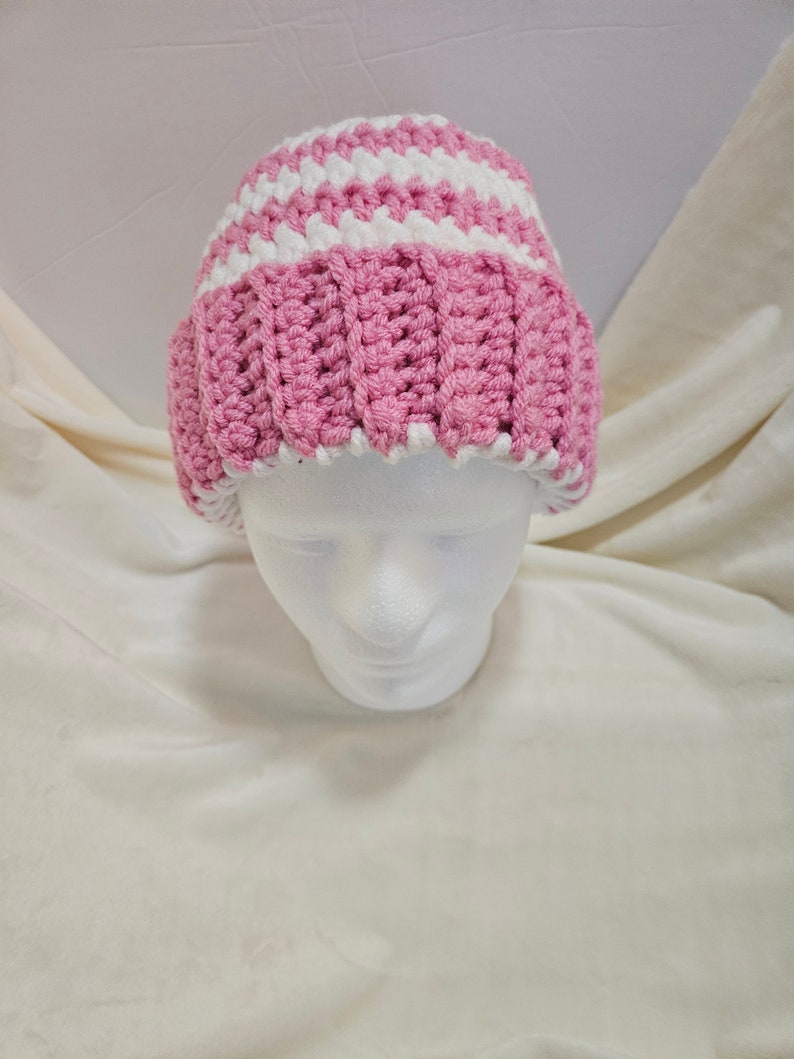 Op de afbeelding: Een roze en witte gestreepte gebreide beanie muts. De muts zit op een wit mannequin hoofd.