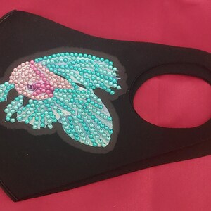 May include: Black face mask with a turquoise and pink fish design made of rhinestones.