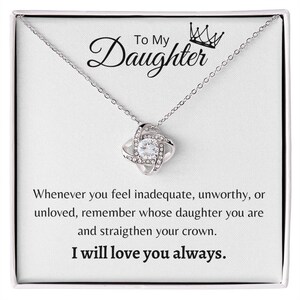 Puede incluir: Un collar de plata con un colgante de nudo y un cristal transparente en el centro. El collar viene en una caja blanca con un mensaje que dice: "A mi hija Siempre que te sientas inadecuada, indigna o no amada, recuerda de quién eres hija y endereza tu corona. Te amaré siempre."