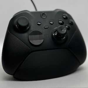 May include: Black Xbox controller featuring multiple buttons, two joysticks, and textured grips. The controller has a sleek design with the Xbox logo on top. A cable extends from the top.