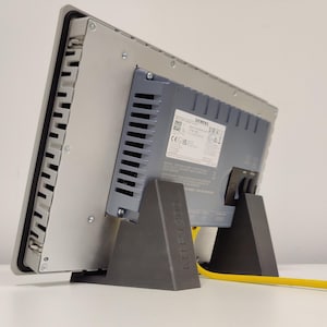 Pode incluir: Um monitor industrial Siemens cinza com um suporte preto e um cabo amarelo. O monitor tem um rótulo com o texto "SIEMENS" e "CE".