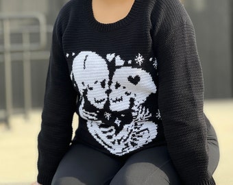 Könnte beinhalten: Schwarzer Strickpullover mit einem weißen Design aus zwei Skeletten, die Herzen halten. Die Skelette tragen Kronen und haben ein Herz zwischen sich.