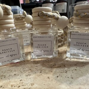 May include: Four clear glass bottles with white labels and gold rope accents. Each bottle has a label that reads "Peach Spritzer oil diffuser" and "KEEWAYDINCANDLES.COM".
