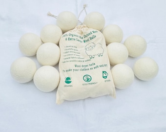 Puede incluir: Un juego de bolas de secado de lana blanquecina con una bolsa de lona. La bolsa está impresa con el texto "100% Organic New Zealand Wool" y "6 Extra Large Wool Balls". La bolsa también tiene un gráfico de oveja e indica que las bolas no contienen químicos.